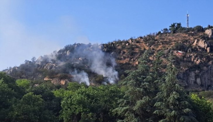 Пламъците горят между скали над малката горичка от западната страна на хълма